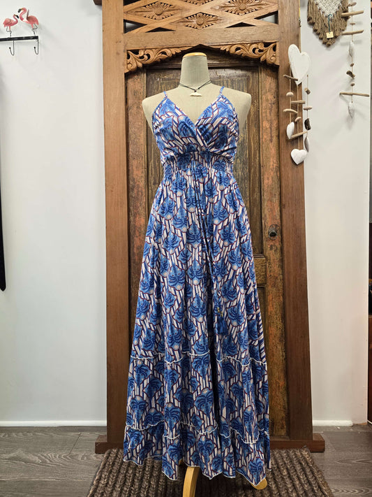 A sleeveless maxi dress with a blue and white abstract pattern, displayed on a mannequin in front of a carved wooden door.