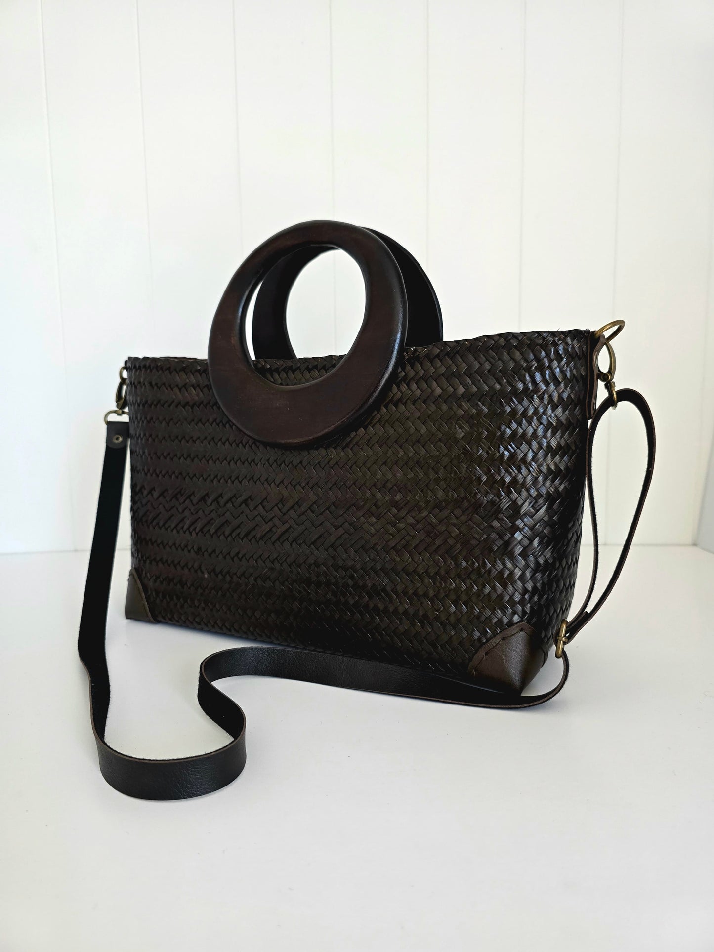 Black woven handbag with a circular wooden handle on a white background