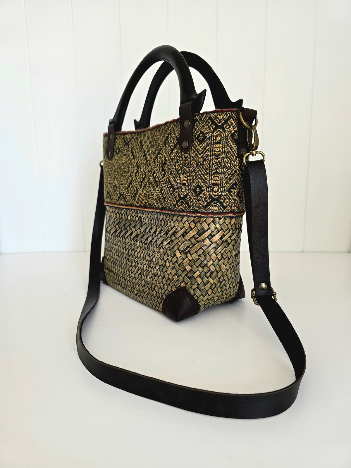 Woven handbag with black strap on a white background