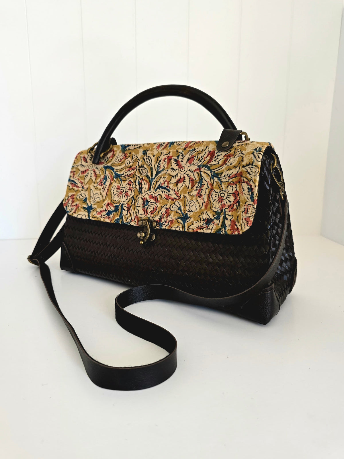 Handbag with floral top flap and black woven body on a white background