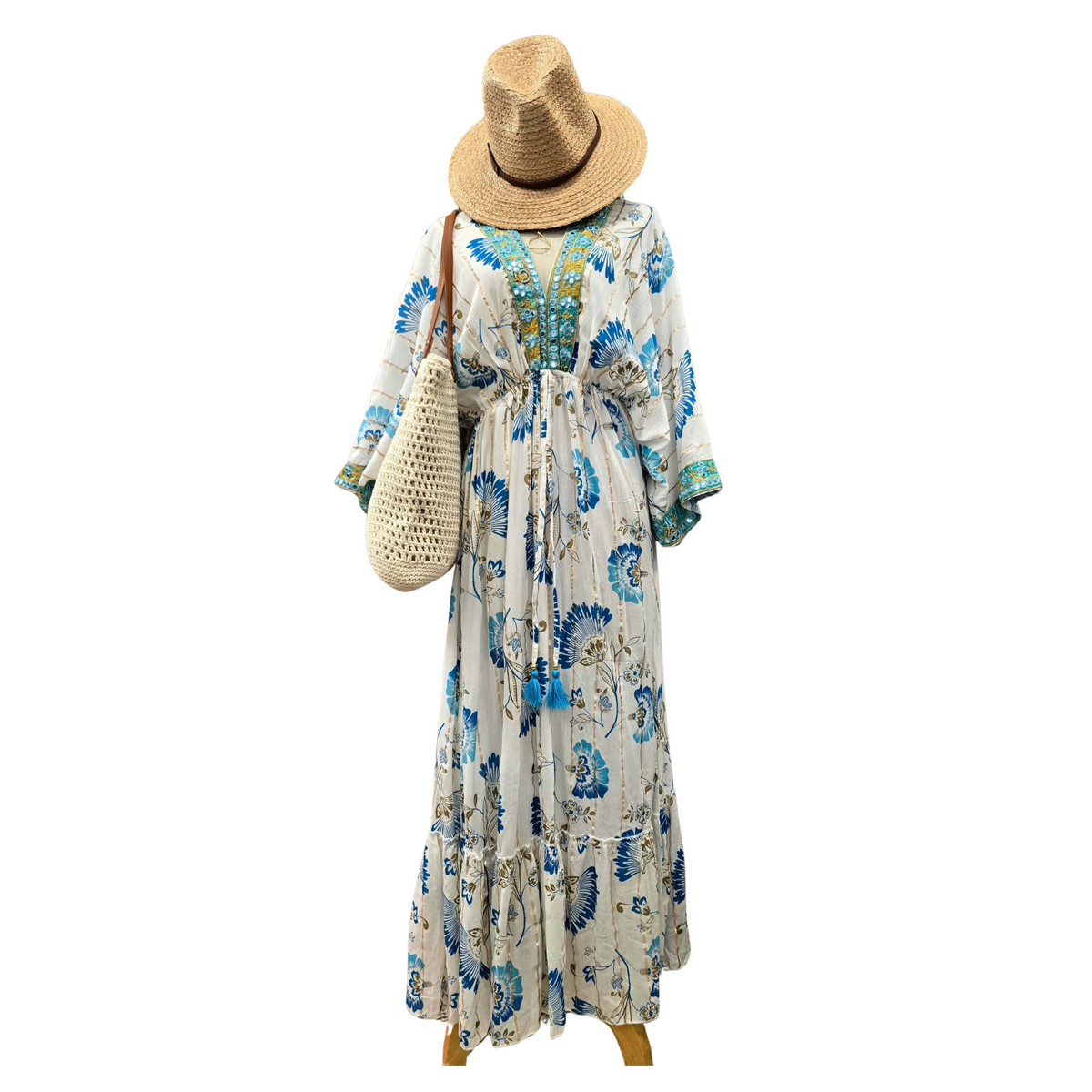 A woman's maxi dress with a blue and green floral print on a cream background, styled with a straw hat, a woven straw shoulder bag, and wooden platform shoes against a plain white background.