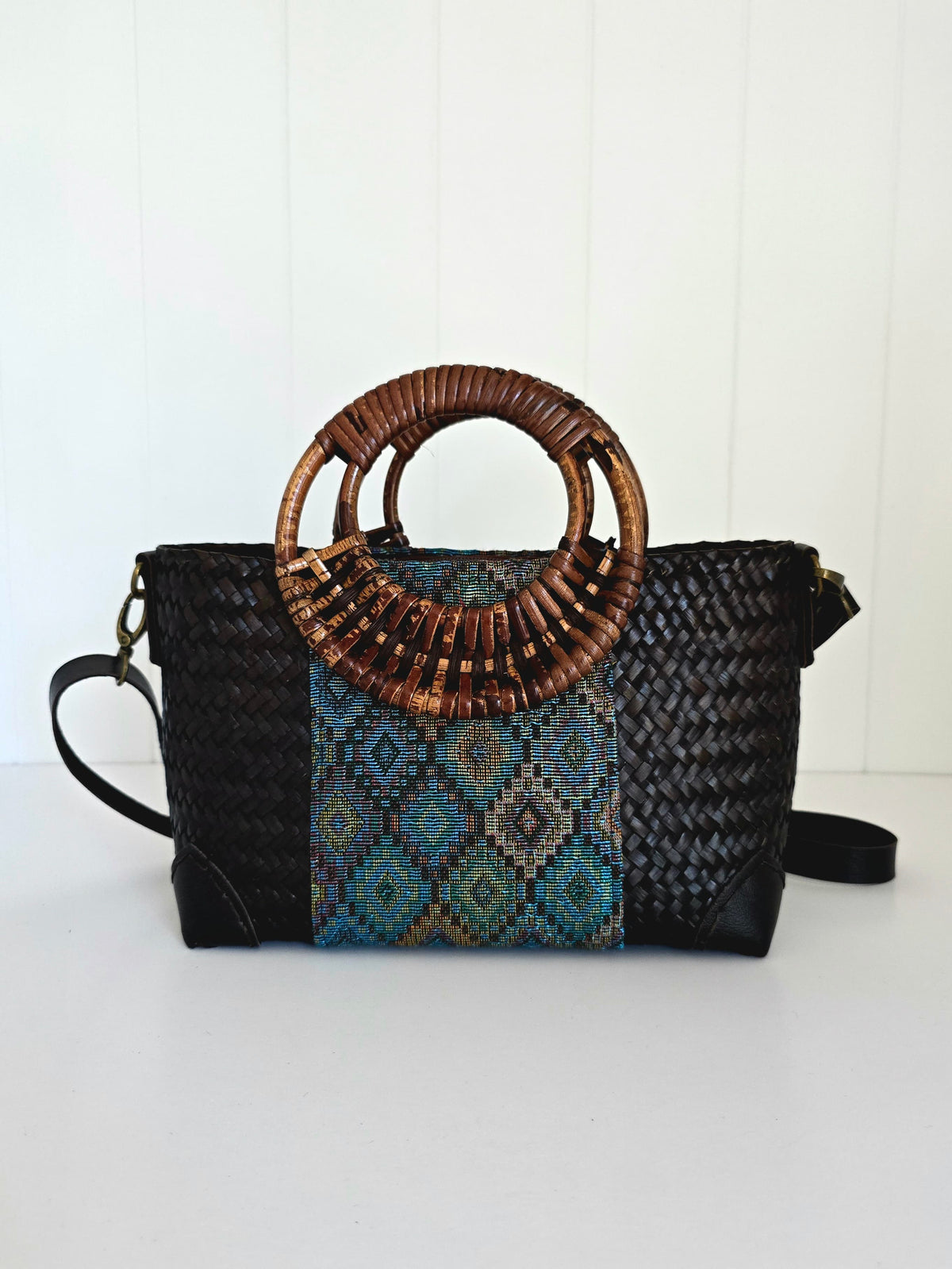 Black handbag with woven top handle and patterned flap on a white background