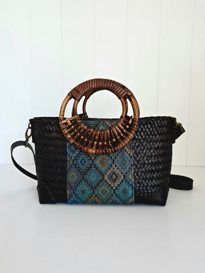 Black handbag with woven top handle and patterned flap on a white background