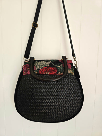 Black woven handbag with floral accents on a white background