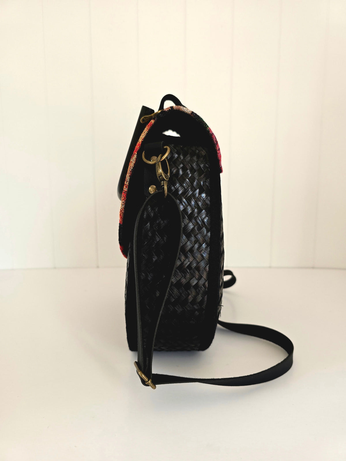 Black woven handbag end view with a strap on a white background