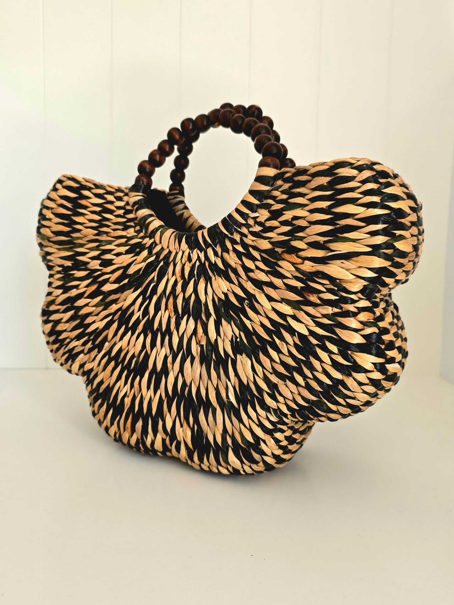 Black and natural colour water grass hand woven together in scallop shape with beaded rounded handles side on