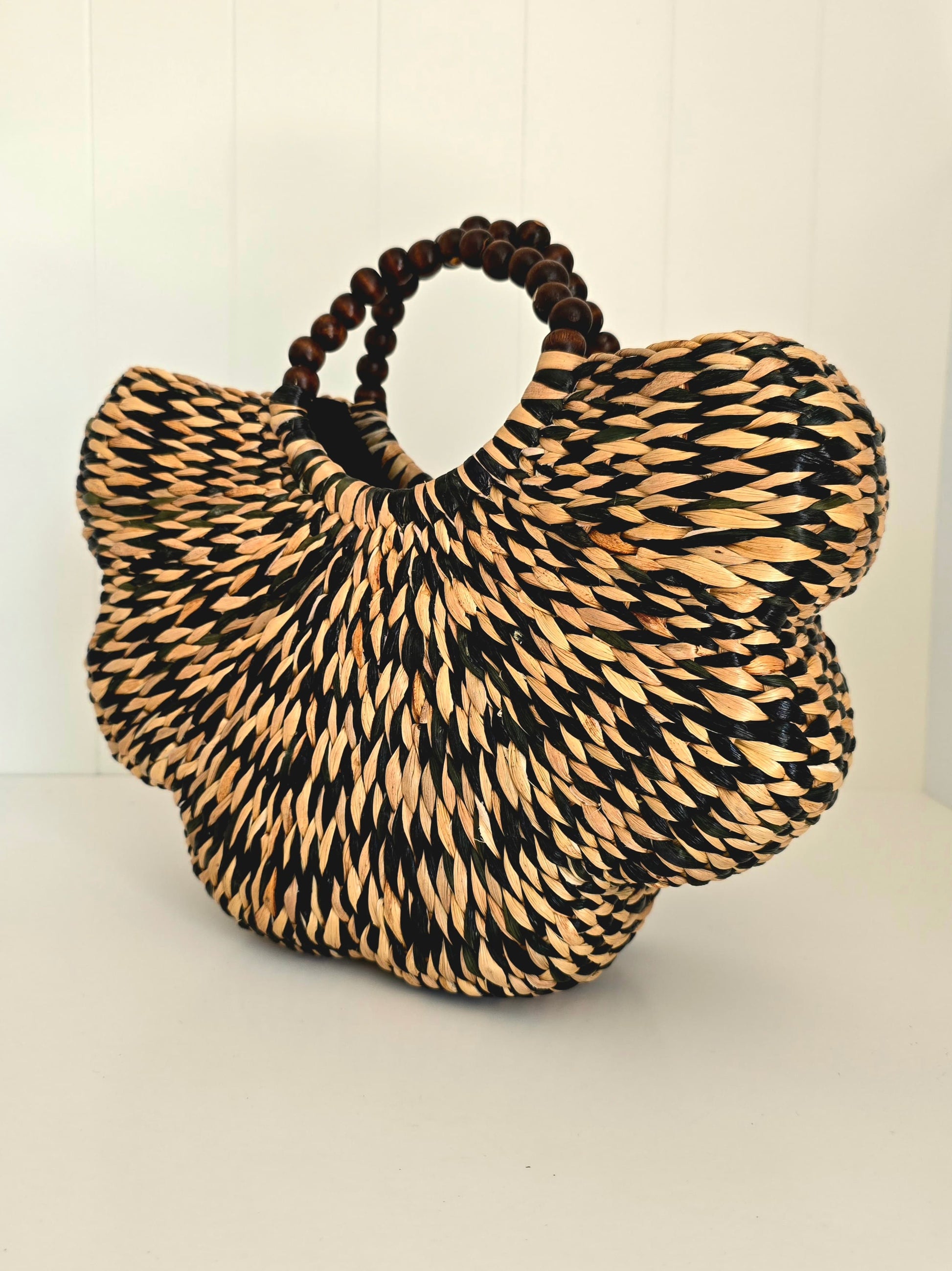 Black and natural colour water grass hand woven together in scallop shape with beaded rounded handles side on