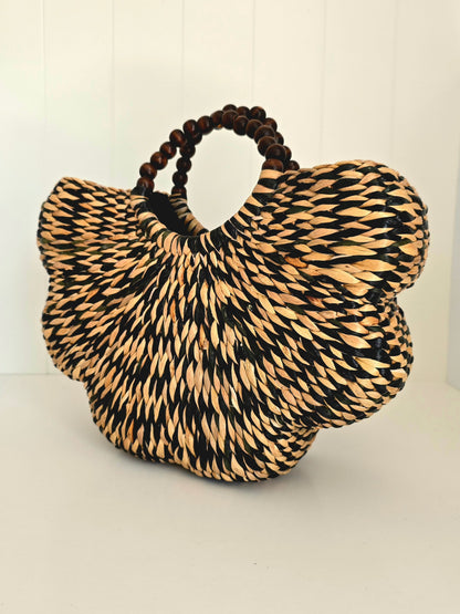 Black and natural colour water grass hand woven together in scallop shape with beaded rounded handles side on