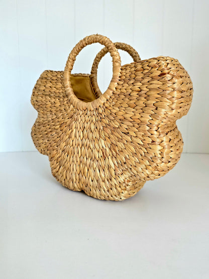 A natural woven straw handbag with a scalloped flower-like silhouette and two top handles, shown on a plain white background.