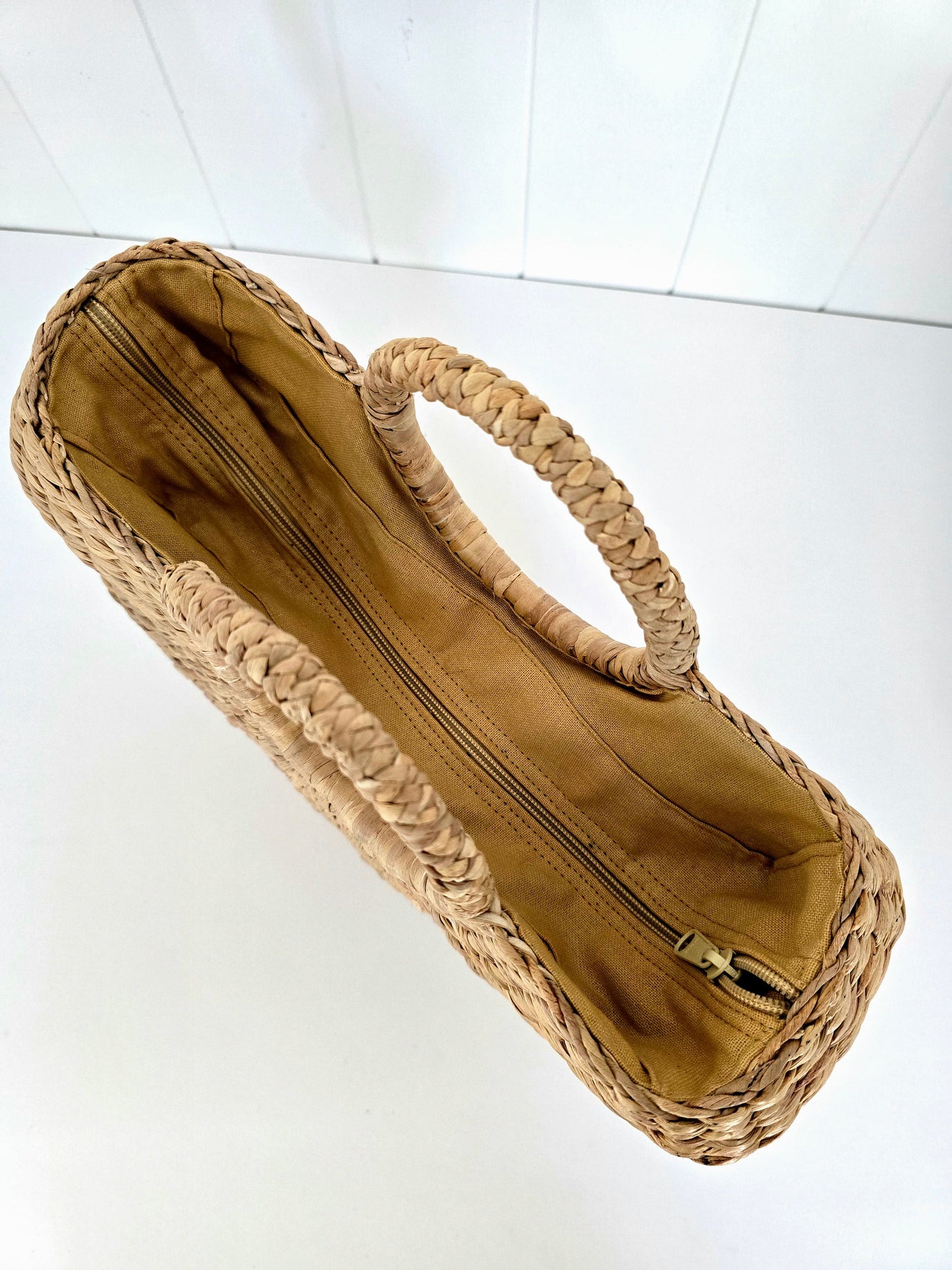 A woven straw handbag with a tan fabric lining and a single integrated top handle, shown from an overhead angle on a white background.