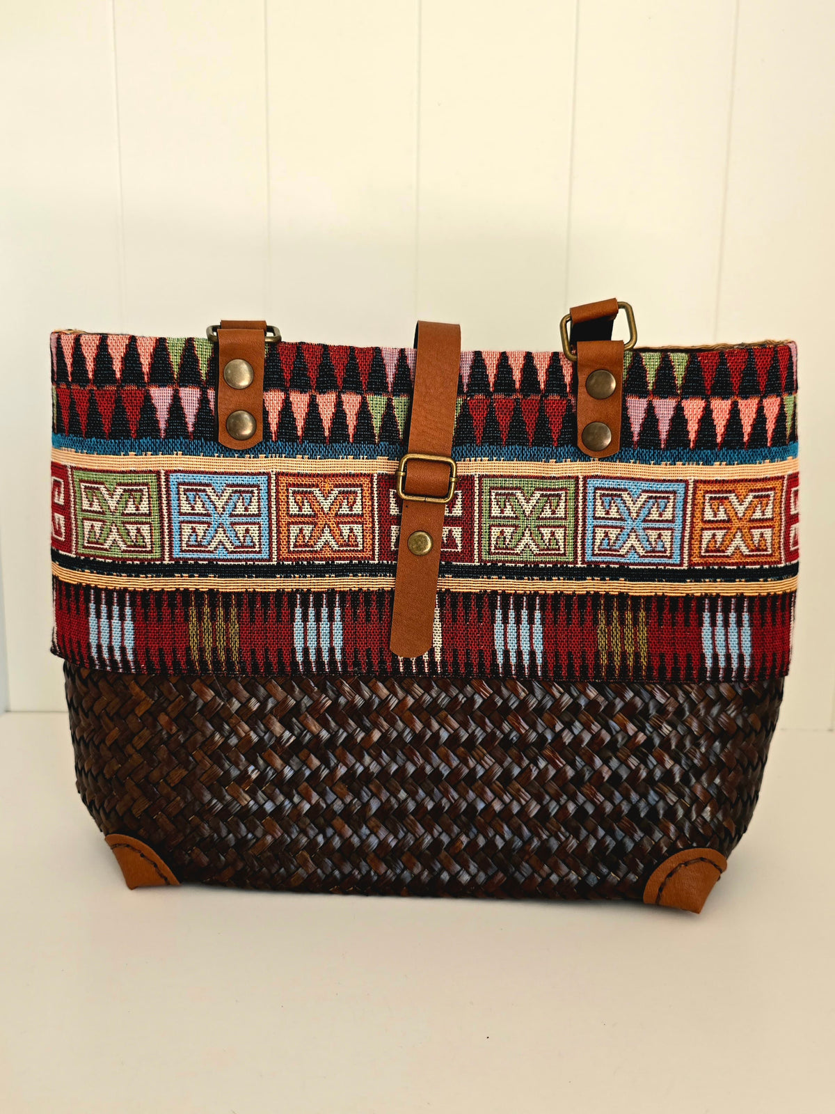 Hand woven Handbag with aztec fabric panel around top.  Faux leather handles and strap to close bag 