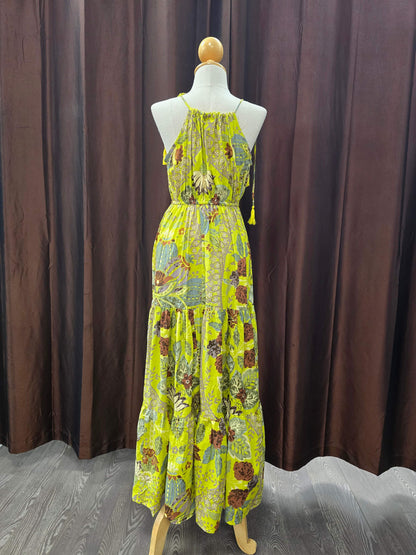 A sleeveless, tiered maxi dress with a vibrant yellow-green base and a multicolor floral and paisley print, displayed on a mannequin in front of a dark brown curtain backdrop.