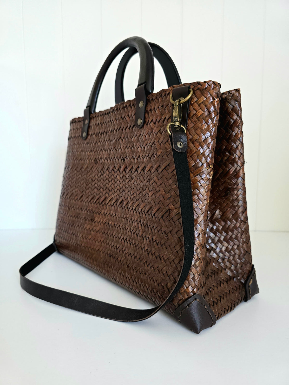 Brown woven handbag with black handle and strap on a white background