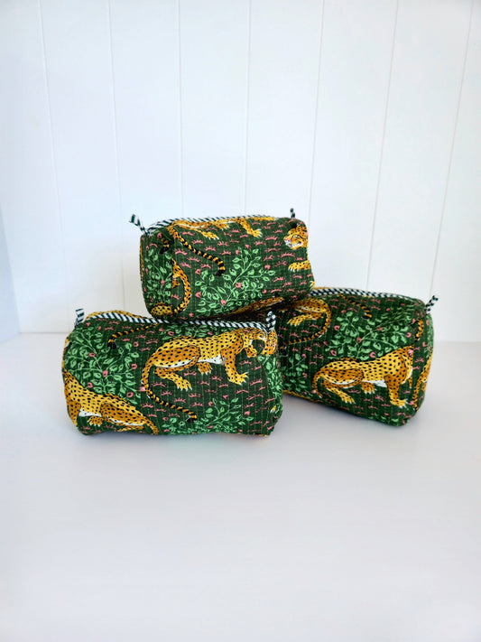 Three small zippered pouches with a green and yellow animal print fabric, arranged on a white surface against a white paneled background.