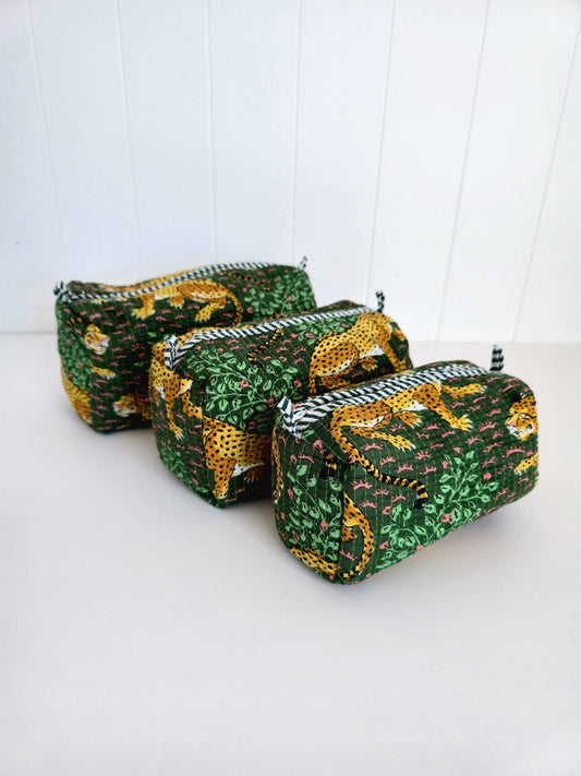 Three small zippered cosmetic pouches in a nested set, featuring a green and yellow leopard print fabric with black and white striped zipper trims, set against a white paneled background.