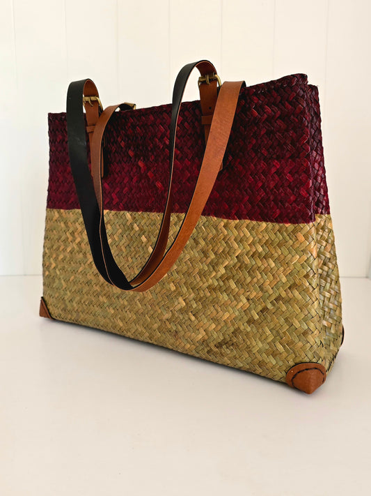 Woven handbag with red top section and natural bottom section on a white background