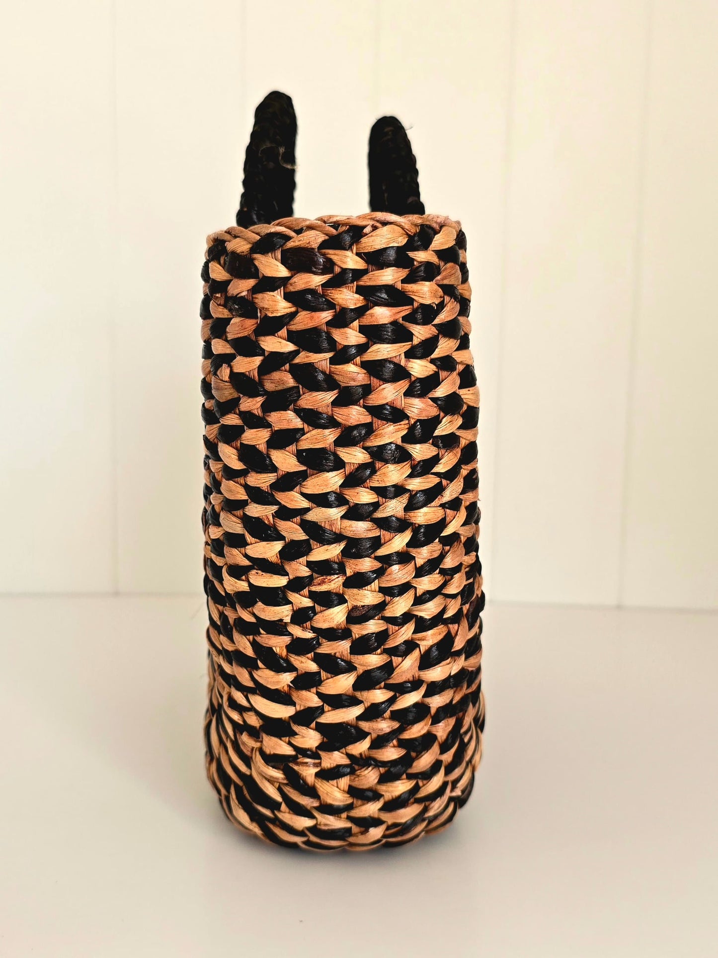 Woven cylindrical basket with black and beige pattern on a white background looking at it from one end