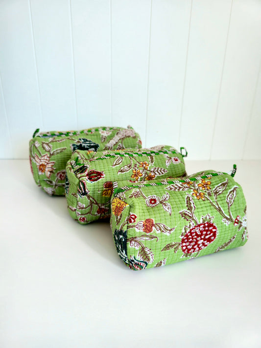 Three small quilted fabric pouches with a green floral botanical print, arranged diagonally on a white surface against a white paneled background.