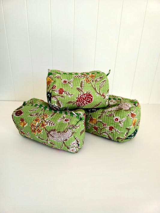Three small zippered fabric pouches with a green floral botanical print, stacked on a white surface against a white paneled background.