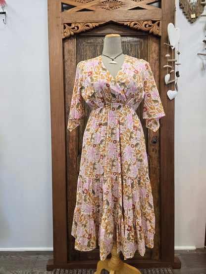A pink and orange floral midi dress with three-quarter sleeves and a V-neckline, displayed on a mannequin torso in front of a carved wooden door.