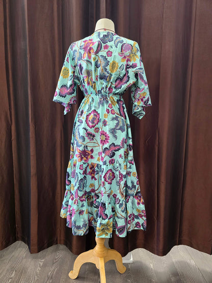 A multicolor floral print midi dress displayed on a wooden dress form mannequin, set against a dark brown curtain backdrop.