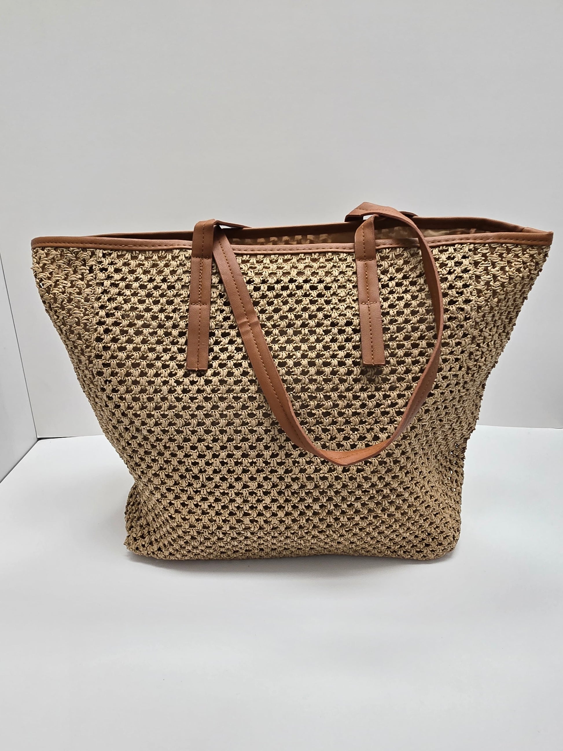 A woven straw tote bag with brown leather handles and trim, photographed against a plain white studio background.