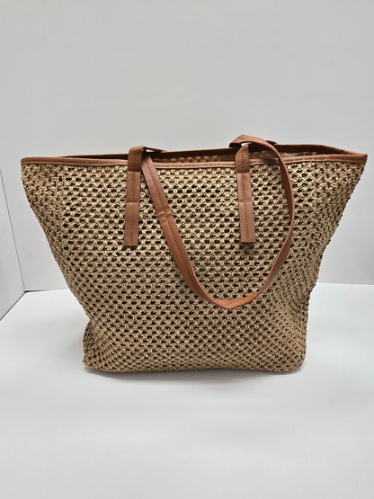 A woven straw tote bag with brown leather handles and trim, photographed against a plain white studio background.