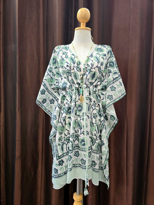 A light green and white floral kaftan tunic with a drawstring waist, displayed on a mannequin torso against a dark brown curtain backdrop.