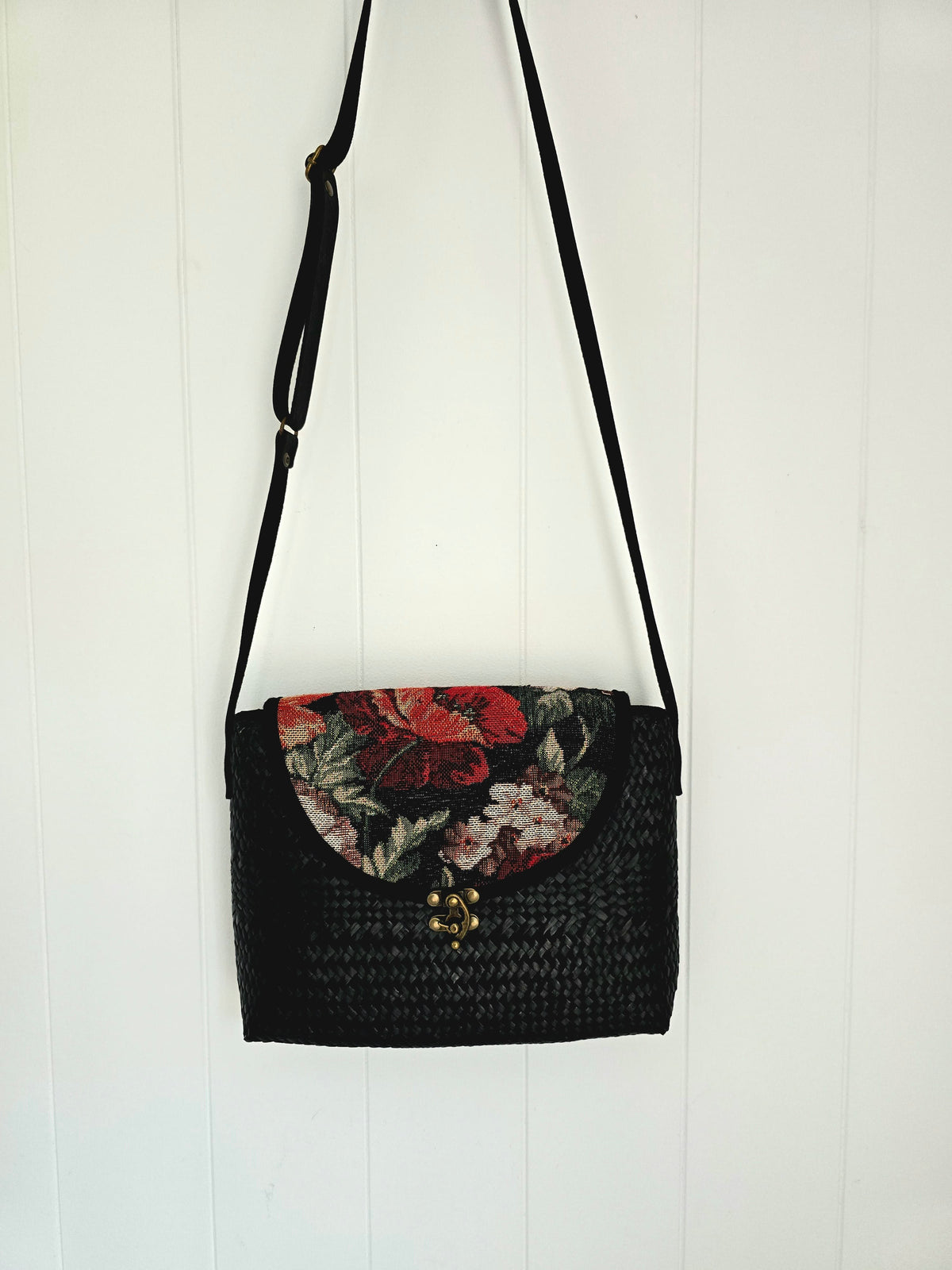 Black woven handbag with floral tapestry design on a white wooden background