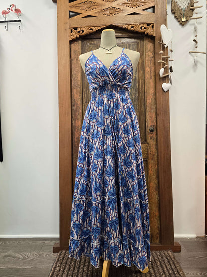 A sleeveless maxi dress with a blue and white abstract pattern, displayed on a mannequin in front of a carved wooden door.