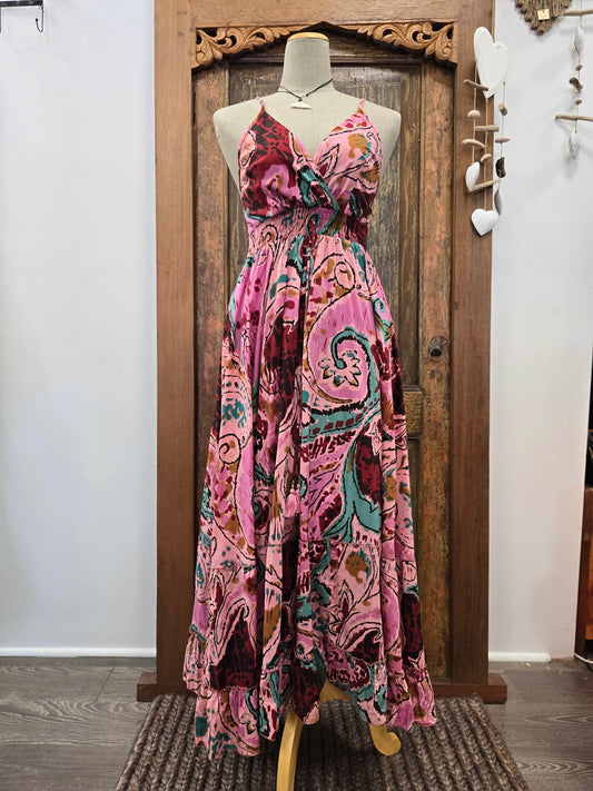 A sleeveless maxi dress with a pink paisley pattern, displayed on a mannequin in front of a rustic wooden door.