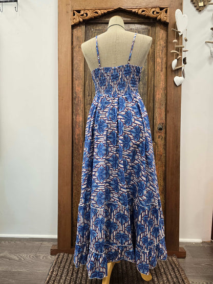 A sleeveless midi dress with a blue and white floral block print, displayed on a beige mannequin torso in front of a rustic wooden door.