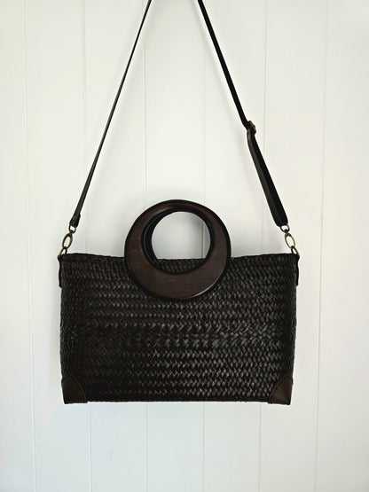 Black woven handbag with wooden ring handle on a white background